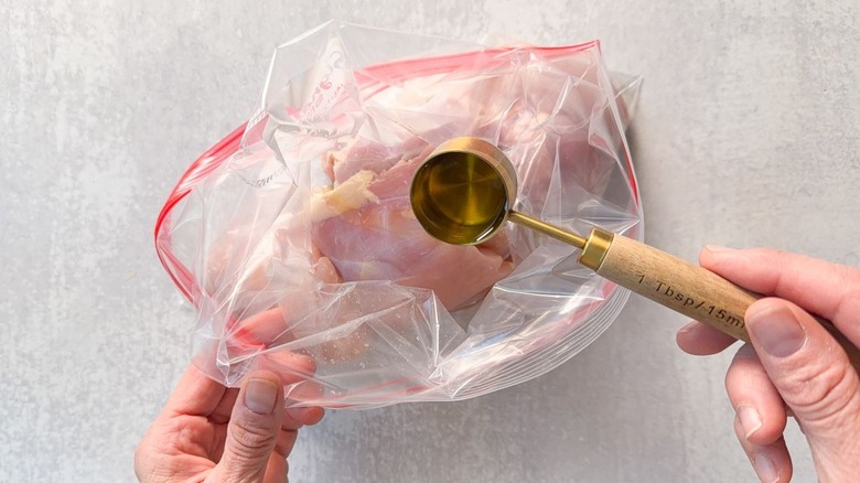 Adding tablespoon of oil to chicken thighs in ziplock bag