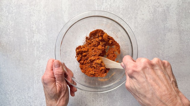 Mixing dry rub spices in glass bowl with wooden spoon