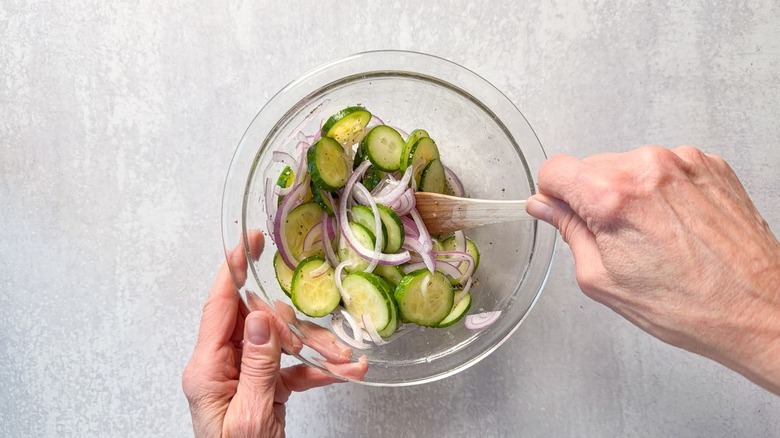 Mixing cucumber and red onion slices with marinade in glass bowl using wooden spoon