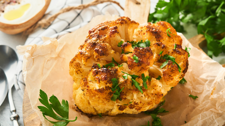 Baked cauliflower. Oven or whole baked cauliflower spices and herbs server on wooden rustic board on old white wooden background table.