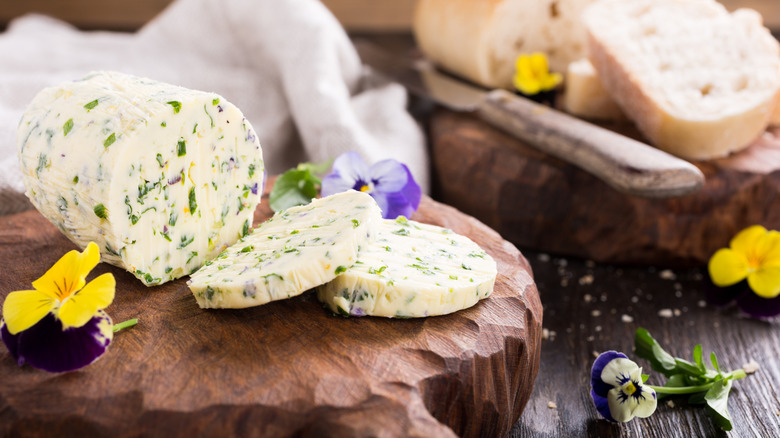 Herb butter log on a cutting board surrounded by edible flowers