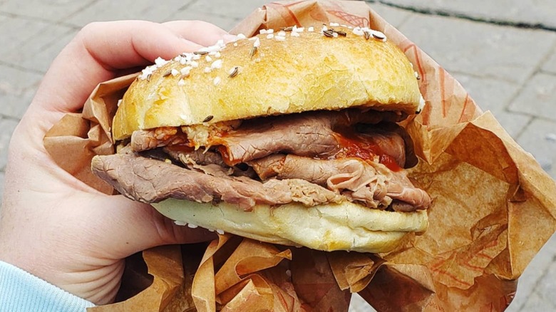 Beef on weck sandwich with French fries and bowl of tomatoes in background