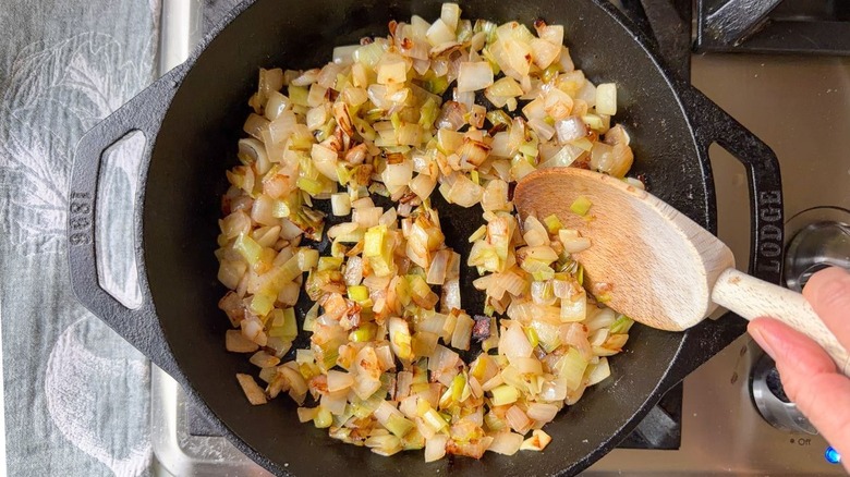 Stirring browned onion, shallot, and leek in cast iron skillet with wooden spoon on stovetop