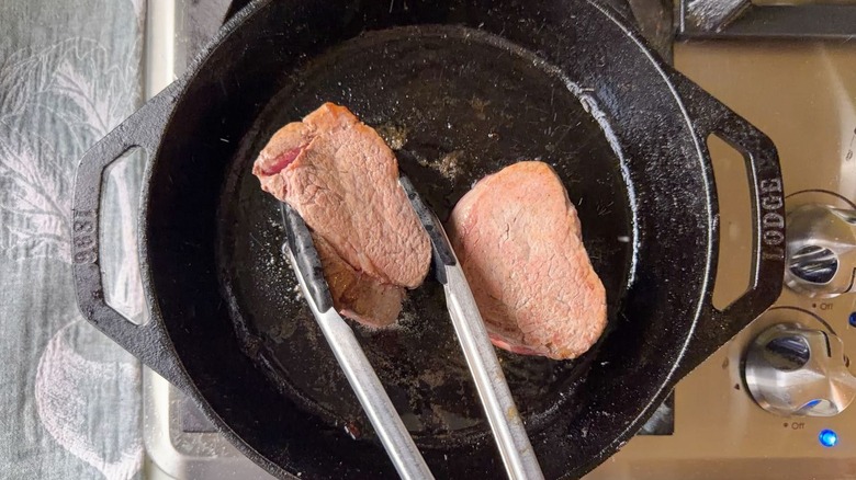 Turning filet mignon in cast iron skillet with tongs