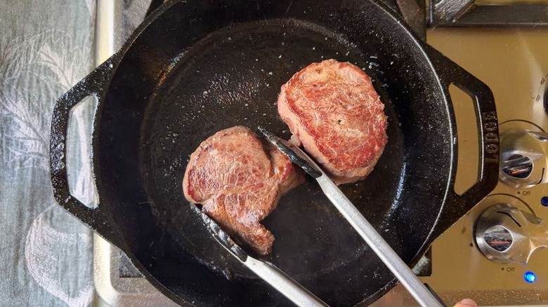 Filet mignon cooking in cast iron skillet with tongs
