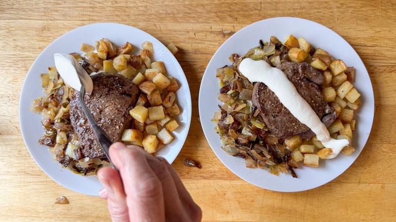 Adding mustard cream to the top of filet mignon with potatoes and onions on plates