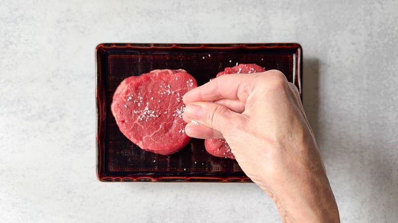 Seasoning filet mignon on plate with salt