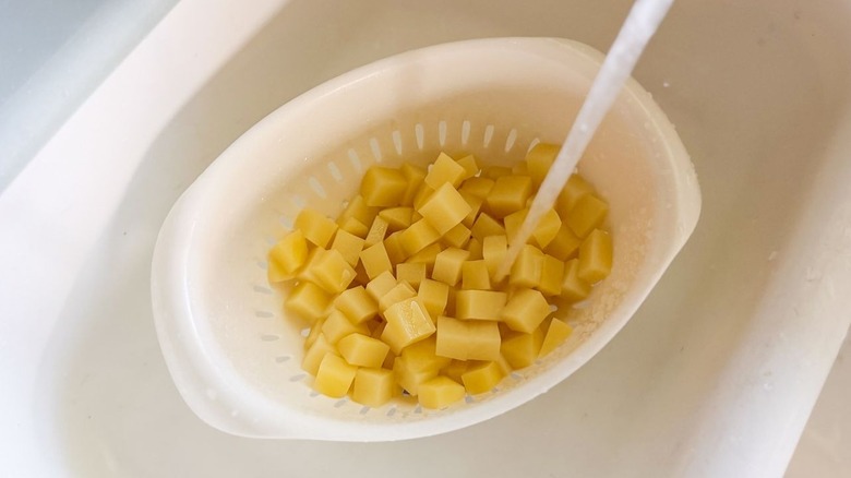 Rinsing potato cubes in colander with water from a faucet