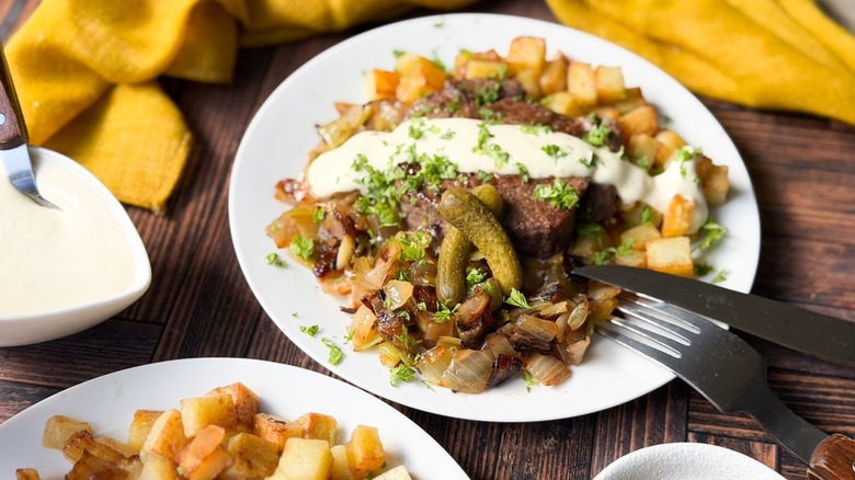 Beef Rydberg-style steak and potatoes on plates with mustard cream sauce, cornichons and red wine