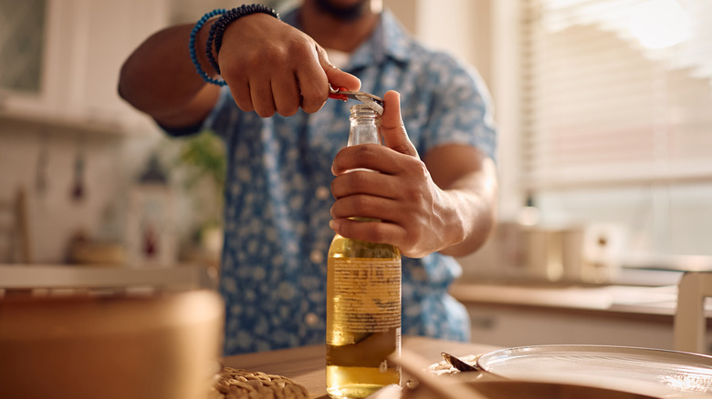 Man popping open a beer bottle with an unidentifiable tool