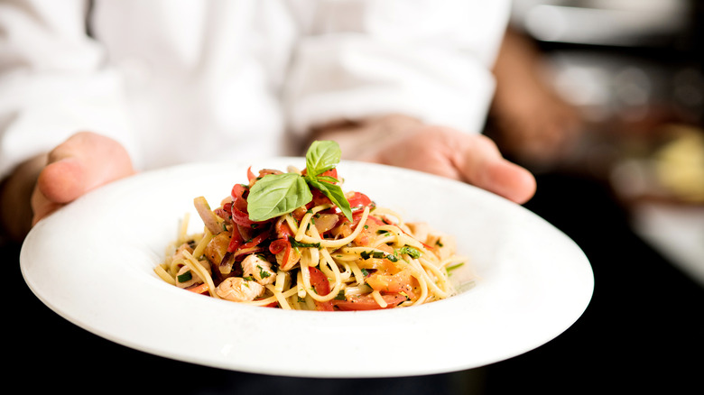 A pasta on a plate being brought out by a server at a restaurant