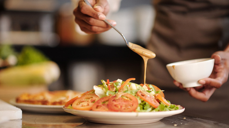 A chef pouring dressing over a fresh bowl of salad.