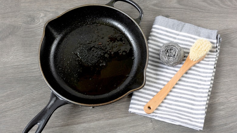 Dish rag and scrub brush beside a dirty cast iron skillet