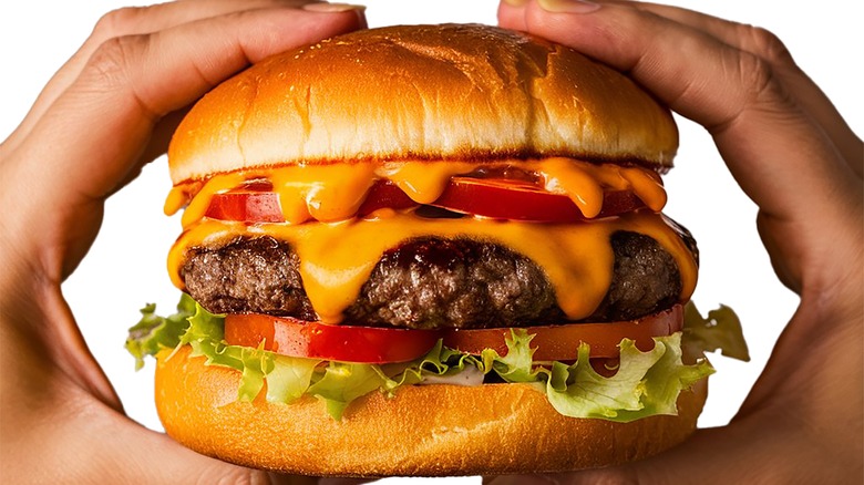 Hands holding a cheeseburger with lettuce and tomato on a toasted bun