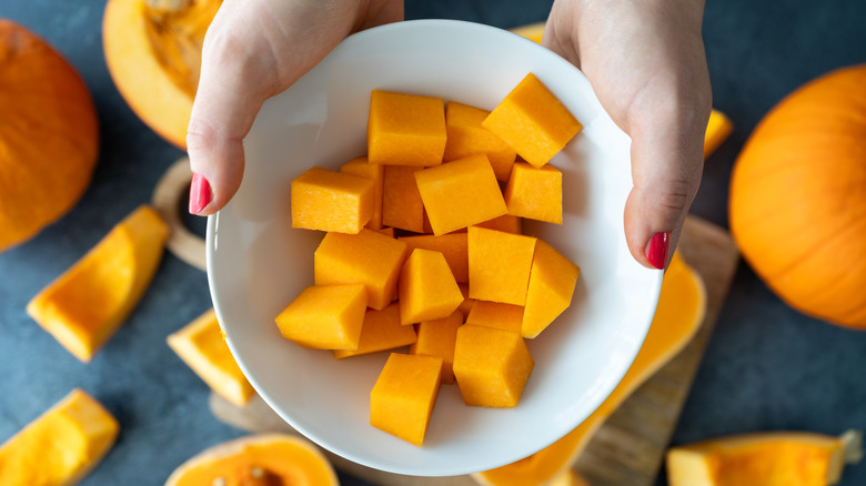 A person's hands are seen holding a white bowl of butternut squash
