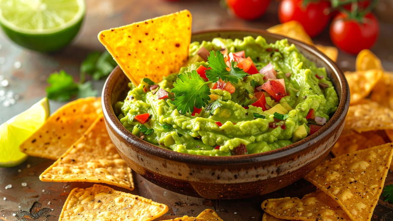 A bowl of fresh guacamole with tortilla chips, cilantro, tomatoes and lime.