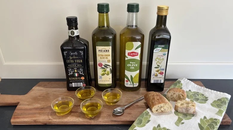 Four different extra virgin olive oils from Aldi sit atop a wooden cutting board