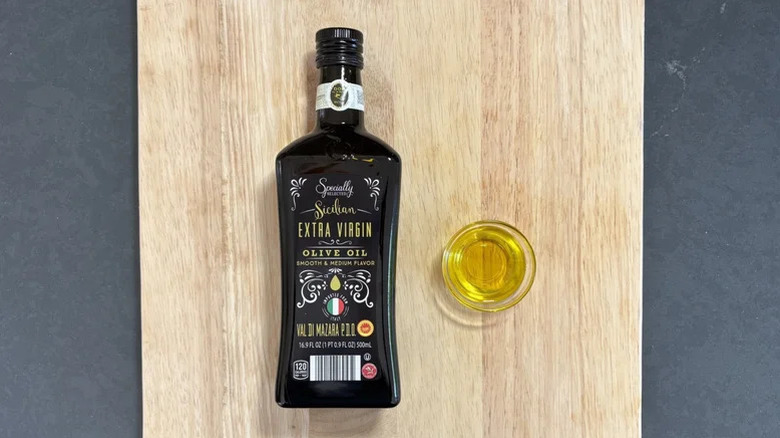 Aldi's Specially Selected Sicilian Extra Virgin Olive Oil lies on top of a wooden cutting board next to small bowl of the oil