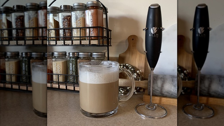 Bean Envy milk frother next to a glass mug of coffee topped with foam