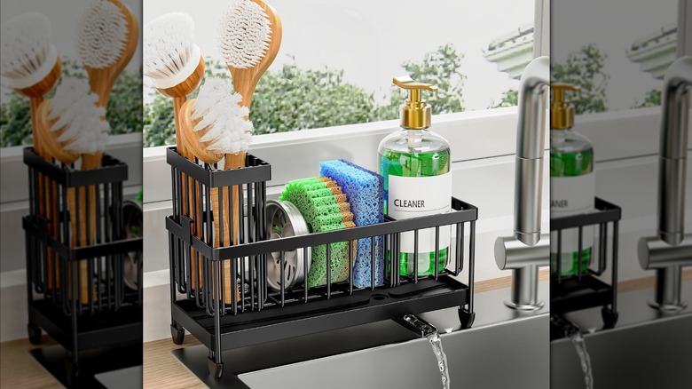 Matte black kitchen sponge organizer with sponges, soap, brushes, and a small spout returning water to the sink