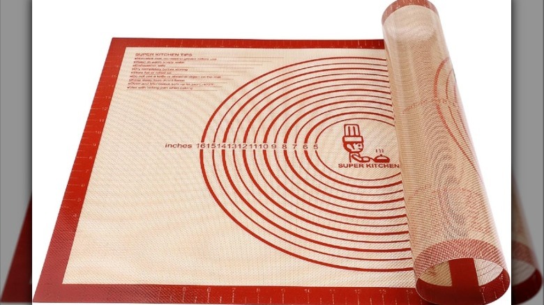 Halfway rolled red and cream colored silicone pastry mat with measurements