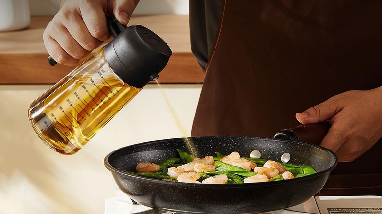 Person praying olive oil into a pan of shrimp and vegetables