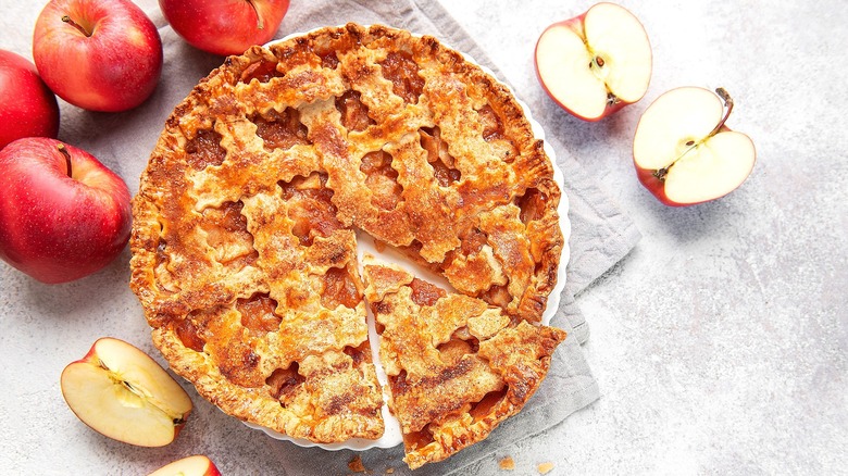 Top-down view of a whole apple pie with lattice crust and a piece cut out