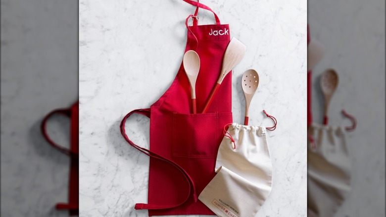 A red apron with Jack embroidered on the top and spatulas in the pocket