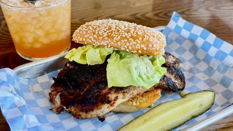 Fishmonger's blackened grouper sandwich nestled in a sesame seed bun, placed on top of a tray with white and blue checkered lining.