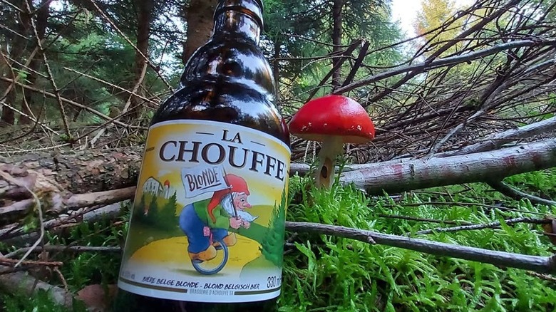 A bottle of La Chouffe Strong Blonde Ale in the forest next to a red mushroom
