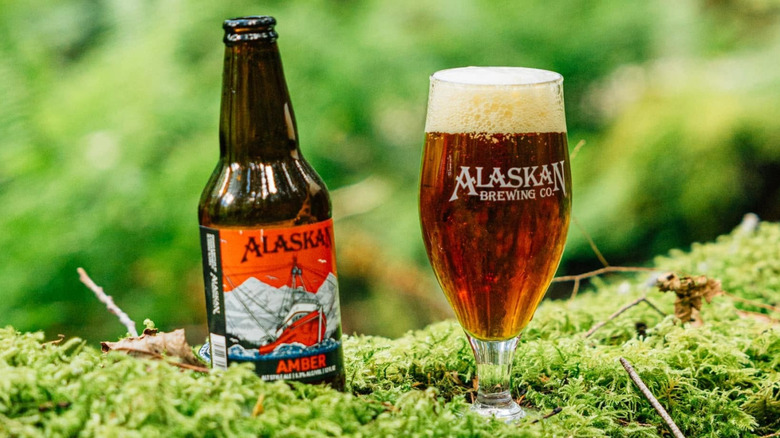 A bottle and glass of Alaskan Brewing Co. Amber Alt-Style Ale sitting on a bed of moss in the forest