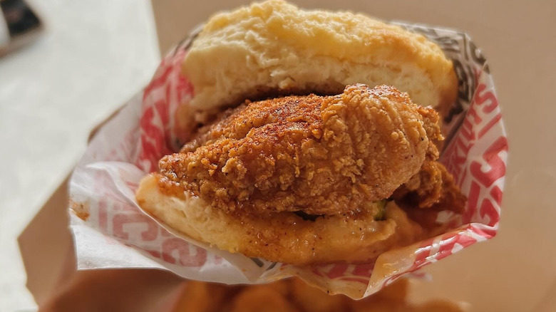 A person holding a fried chicken biscuit sandwich from District Biskuits