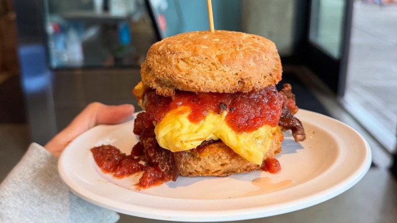 A person holding a biscuit sandwich on a plate at Morsel
