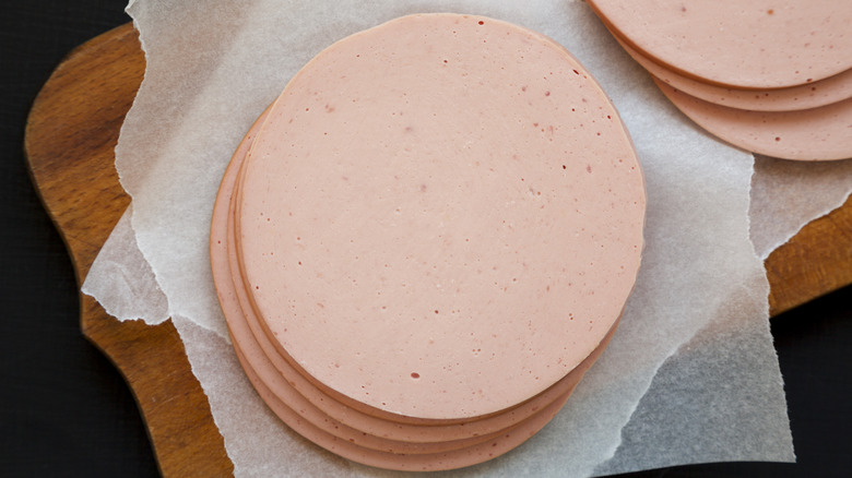 Sliced bologna on parchment paper on wooden board