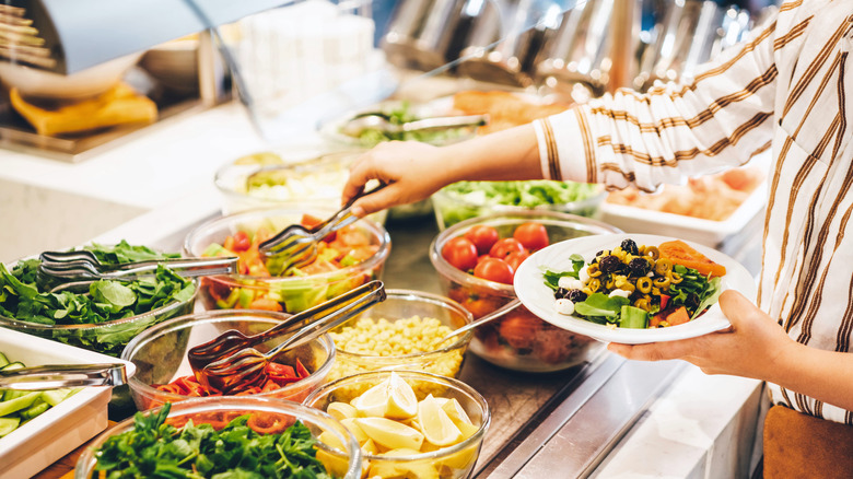 A person creating a salad plate at a buffet