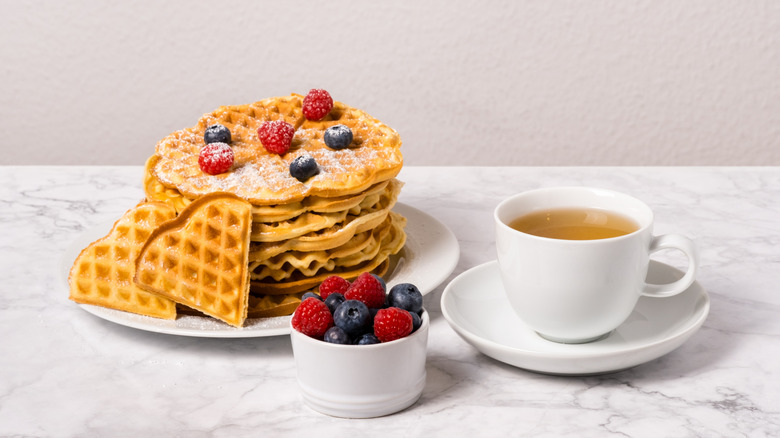Stack of waffles topped with powdered sugar and berries with a cup of tea