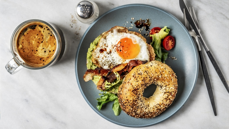 A bagel breakfast sandwich on a plate next to a cup of coffee