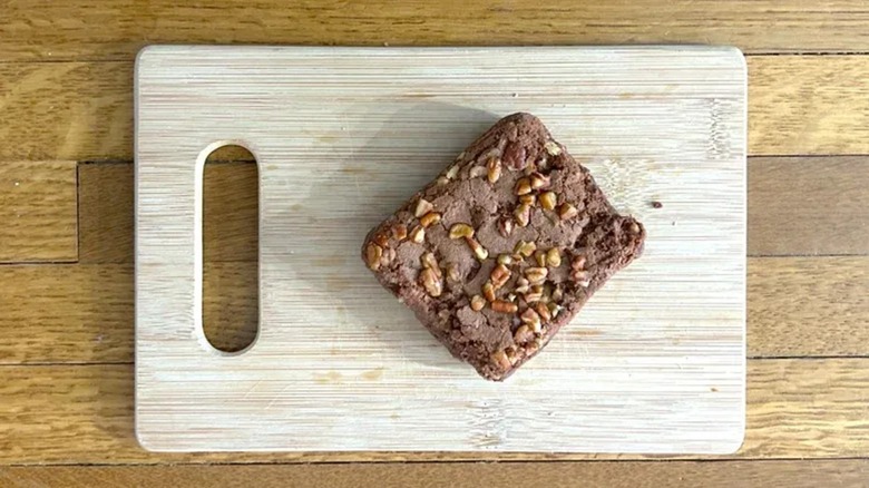 A piece of brownie with nuts on a wooden board