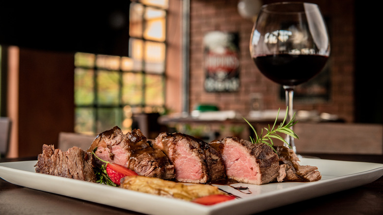 Steak sliced into pieces on a plate next to a glass of wine