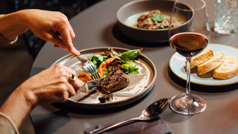 Hands cutting steak on a plate at a restaurant