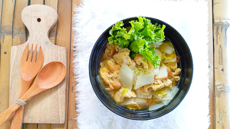 A bowl of soup made with cabbage next to wooden silverware