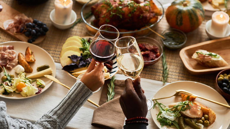 Two people toasting their glasses at a table full of comfort foods