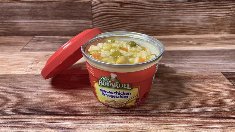 An opened microwaveable can of Chef Boyardee Rice with Chicken & Vegetables sitting on a wooden table