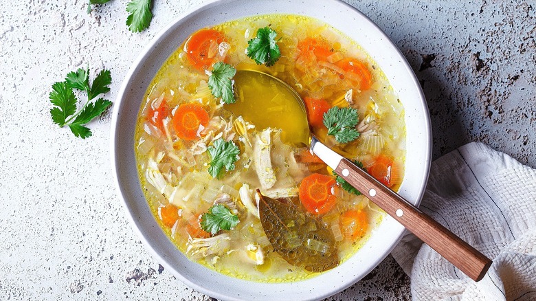 Chicken soup with sliced carrots and fresh parsley in a shallow white bowl with a spoon