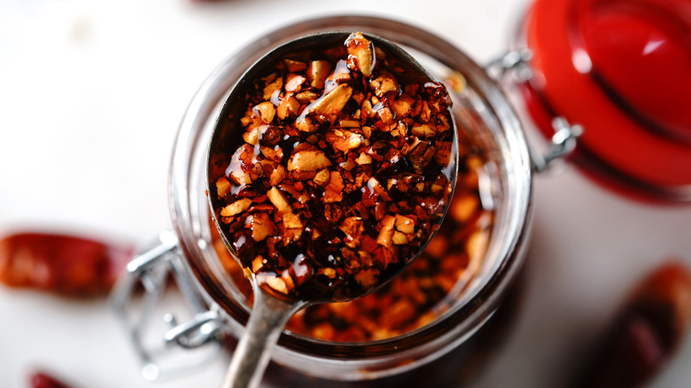 A spoonful of chili crisp with a jar of chili crisp blurred in the background under the spoon