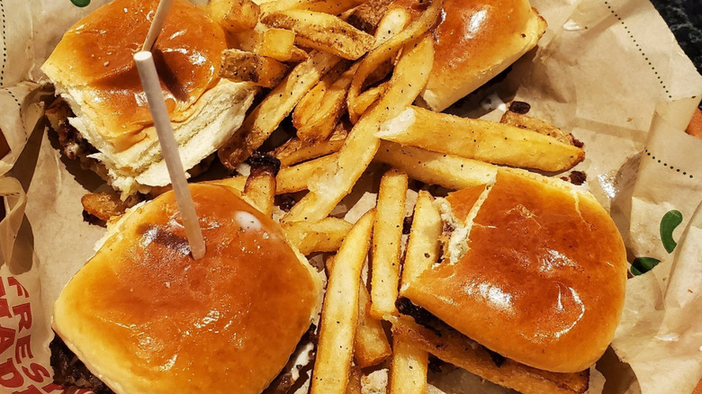 Four mini burgers, each with a stick, and a hefty serving of thick-cut fries in the middle