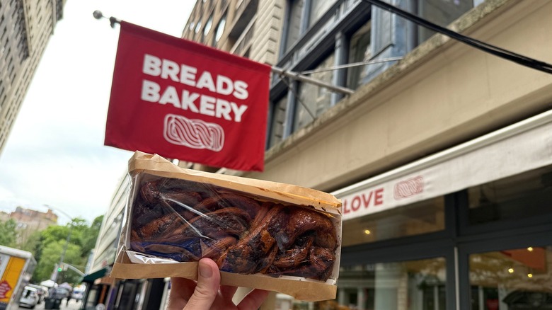 a babka held below the Breads Bakery flag