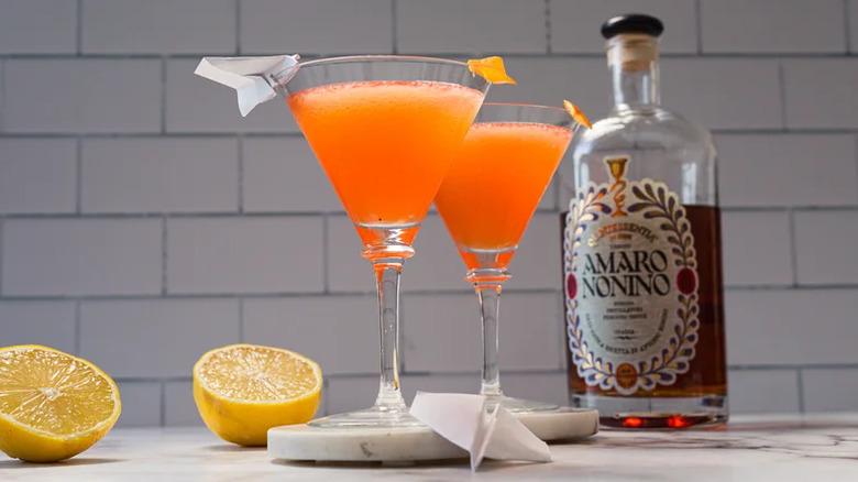 Two Paper Plane cocktails in martini glasses with a bottle of amaro in the background
