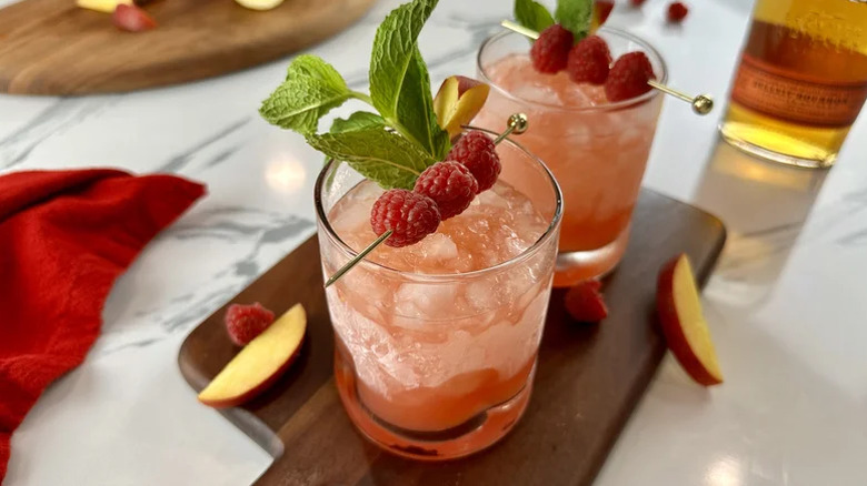 Two glasses of peach and raspberry bourbon smash with fresh raspberry garnish