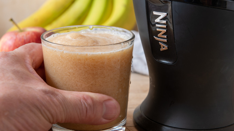 A person holding a glass of fresh juice next to a Ninja juicer